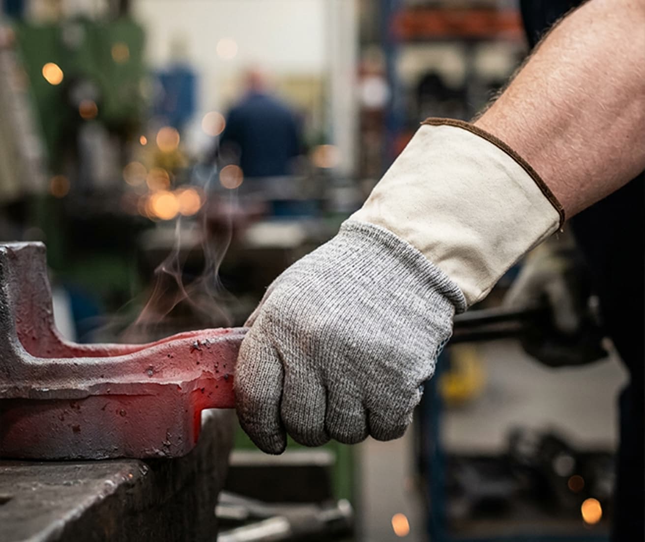 Pracownik w rękawicach ochronnych chwytający rozgrzany metal w warsztacie metalurgicznym